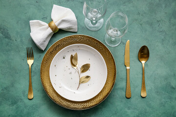 Elegant table setting with golden leaves and cutlery on green table