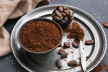 Bowls with cocoa powder and beans on black background