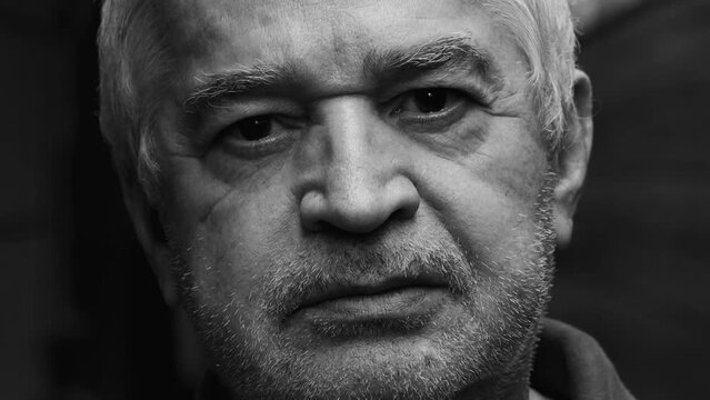 Dramatic portrait of a wrinkled senior man close-up face in monochromatic black and white photography staring at camera with stern concerned expression