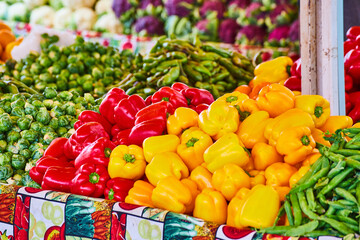 Red and yellow bell peppers and variety of other vegetables on tables