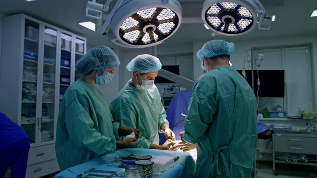 Three male surgeons carrying out the operation in modern clinics. Female nurse assisting the doctors preparing tools for them.