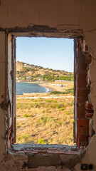 Fototapeta premium Window to the sea in an abandoned house across to Kalekoy sea town. The Aegean sea town view from window. Gokceada, Imbros island, Canakkale.