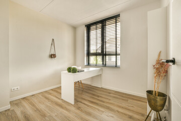 a room with wood flooring and white walls, there is a plant on the table in front of the window