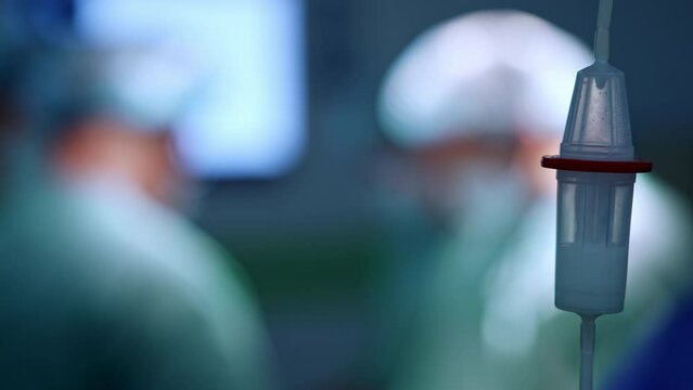 Drops of medicines fall inside the reservoir of drop counter. Close up. Doctors work in surgery room at blurred backdrop.