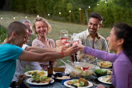 Group of middle-aged friends dining together on the terrace of a house or restaurant. Happy people eating and drinking toast at an outdoor table, sharing and enjoying time together. High quality photo