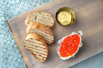 Salmon red caviar in an oyster shell with butter and toast on a blue background. Mediterranean...