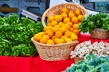 Oranges in wicker baskets next to vegetables at farmers market