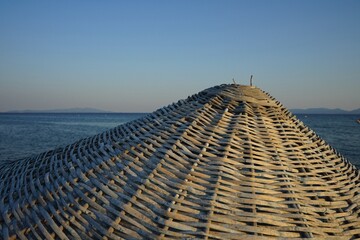 Große runde Sonnenschirme aus Korbgeflecht vor blauem Himmel im Licht der Abendsonne im Sommer am...