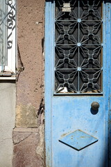 Vergittertes Fenster einer Stahltür in Blau mit Rost und Patina eines heruntergekommenen Altbau im...