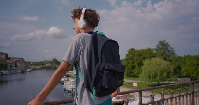 A teenager guy on the background of a beautiful old city in headphones travels around the city and listens to music