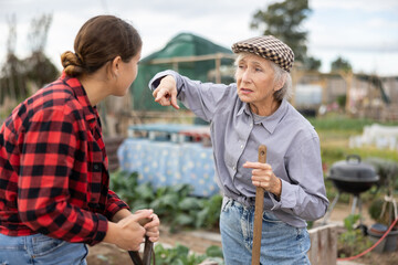 Two angry casual women neighbors of different ages arguing during the vegetable garden season on sunny day of spring