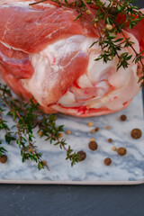 Pork knuckle.Farm organic meat. Pork meat on the bone.Pork knuckle, peppercorns, fresh thyme on a marble board on a black slate background.
