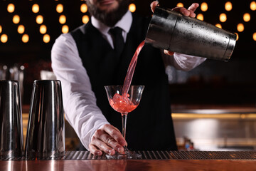 Bartender preparing fresh alcoholic cocktail in martini glass at bar counter, closeup