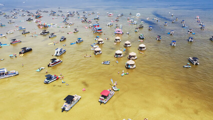 Fototapeta na wymiar Crowd of people at Crab Island in Destin, Florida during low tide with brown brackish water, busy pontoons, jet skis, paddleboards, swimming, wading activities at shallow water