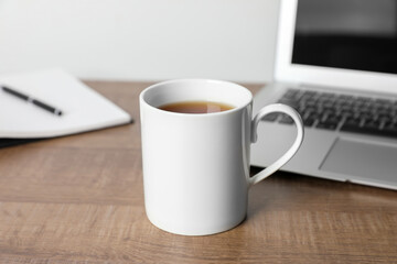 White ceramic mug with drink, notebook and laptop on wooden table at workspace