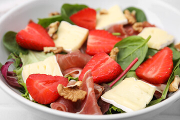 Tasty salad with brie cheese, prosciutto, strawberries and walnuts in bowl, closeup