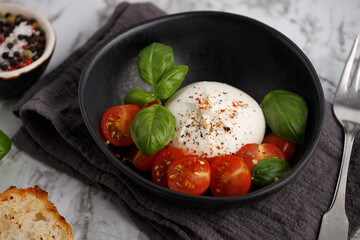 Italian burrata with tomatoes and basil on plate on marble table, close up.