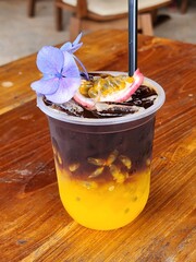 Ice americano with orange juice  and passion fruit  on top. Decorate ith  Flower .The cup put on the old wood table