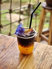 Ice americano with orange juice  and passion fruit  on top. Decorate ith  Flower .The cup put on the old wood table