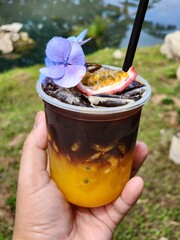Ice americano with orange juice  and passion fruit  on top. Decorate ith  Flower .The cup put on the old wood table