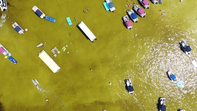 Close-up aerial dense of pontoon, boat rentals, jet skis, paddleboards, swimming, wading activities at low tide shallow brackish water of Crab Island, Destin, Florida