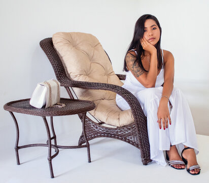 Mulher sentada tomando uma tar&ccedil;a de vinho em um sen&aacute;rio clean, com um lindo vestido branco.