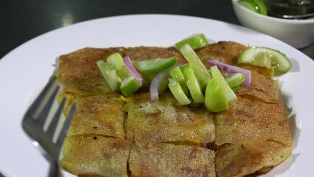 chicken Mataba on a white plate and a bowl of dipping sauce next to it. All This Menu is on stainless surface table.