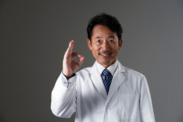 OKポーズをするミドルエイジの医者　黒背景