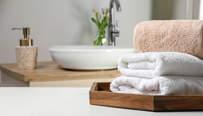 Wooden tray with stacked bath towels and beautiful flowers on white table in bathroom. Space for text