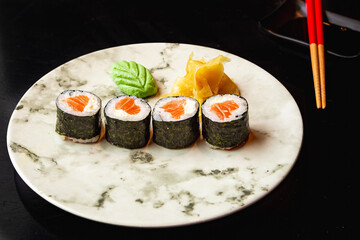 Japanese food| sushi platter, salmon hossomaki with soy sauce and chopsticks on a black table.