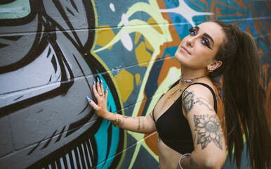 Beautiful young woman with tattoos and street graffiti