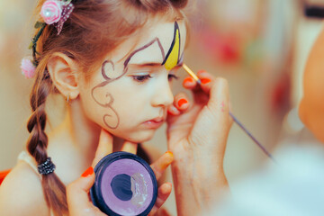 Little Girl Having her Face Painted at a Kids Party Event. Entertainment artist creating a make-up...