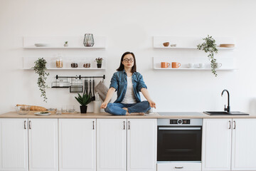 Woman meditating while sitting on white designer kitchen set
