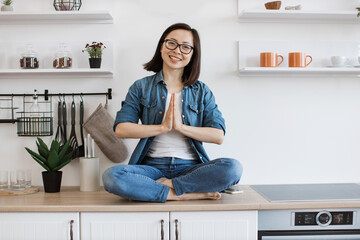 Woman sitting in lotus position with namaste on work surface