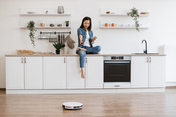 Lady with phone programming robot vacuum for tidying kitchen