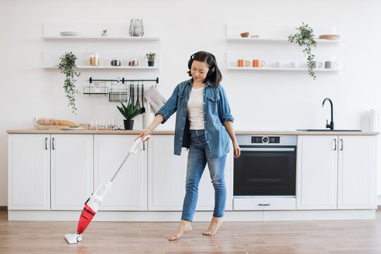 Asian lady using upright vacuum with music in headphones