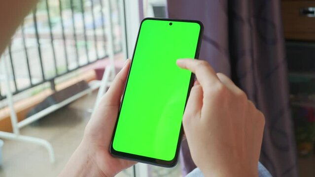 Woman holding smartphone in hands and scrolling with green screen.
