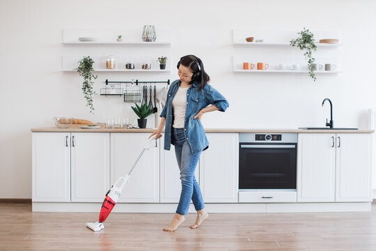 Asian lady using upright vacuum with music in headphones