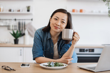 Asian woman drinking water after snack while teleworking
