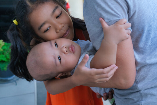 Young Asian girl playing with her baby brother in her grandma's arms