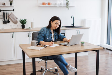 Busy woman surfing internet on computer at kitchen table
