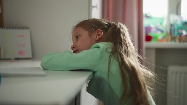 Sad little girl rests while doing homework at desk in children room. Tired schoolgirl lies on table procrastinating boring tasks completion at home