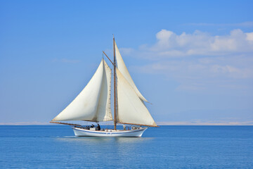 Fototapeta premium A sailboat on a calm blue sea, two white sails, blue sky