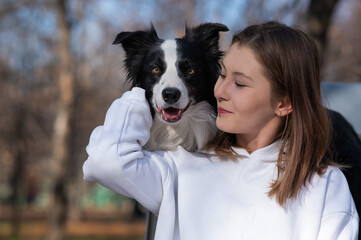 Caucasian woman hugging her dog Border Collie while sitting on a bench in autumn park.