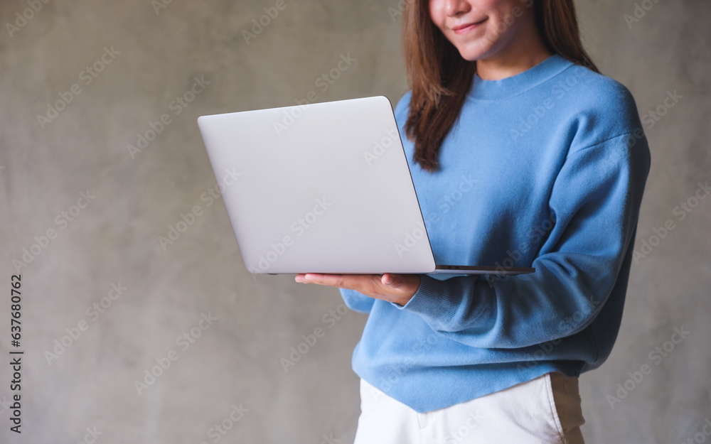 Wall mural Closeup image of a young woman holding and working on laptop computer