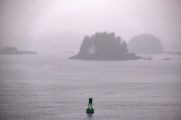 Grey, misty, foggy morning in archipelago near Sitka, Alaska with small islands channel cruising...