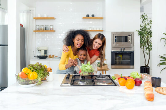 Two women a child, cooking together in a well-lit, homey kitchen, standing before a modern stove, embodying unity, love and tradition. - Powered by Adobe