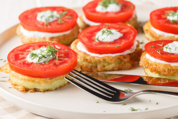 Zucchini in egg batter served with tzatziki sauce and fresh tomatoes close-up in a plate on the...