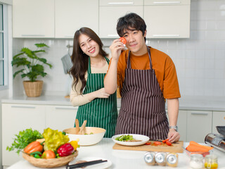 Asian young lover couple husband and wife in casual outfit with apron standing smiling in full decorated modern kitchen at home