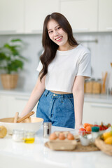 Obraz na płótnie Canvas Asian young beautiful housewife in casual outfit standing smiling posingt in full decorated modern kitchen with ingredients and equipment.